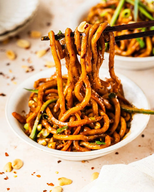 A bowl of thick noodles with visually appealing sauce on a dining table